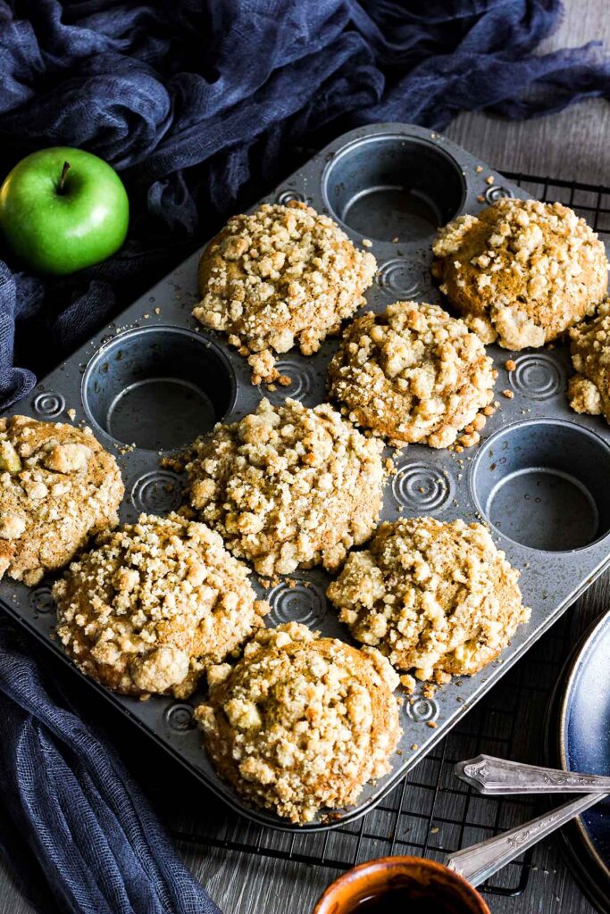 Pan of apple muffins with a few missing and an apple on the side.