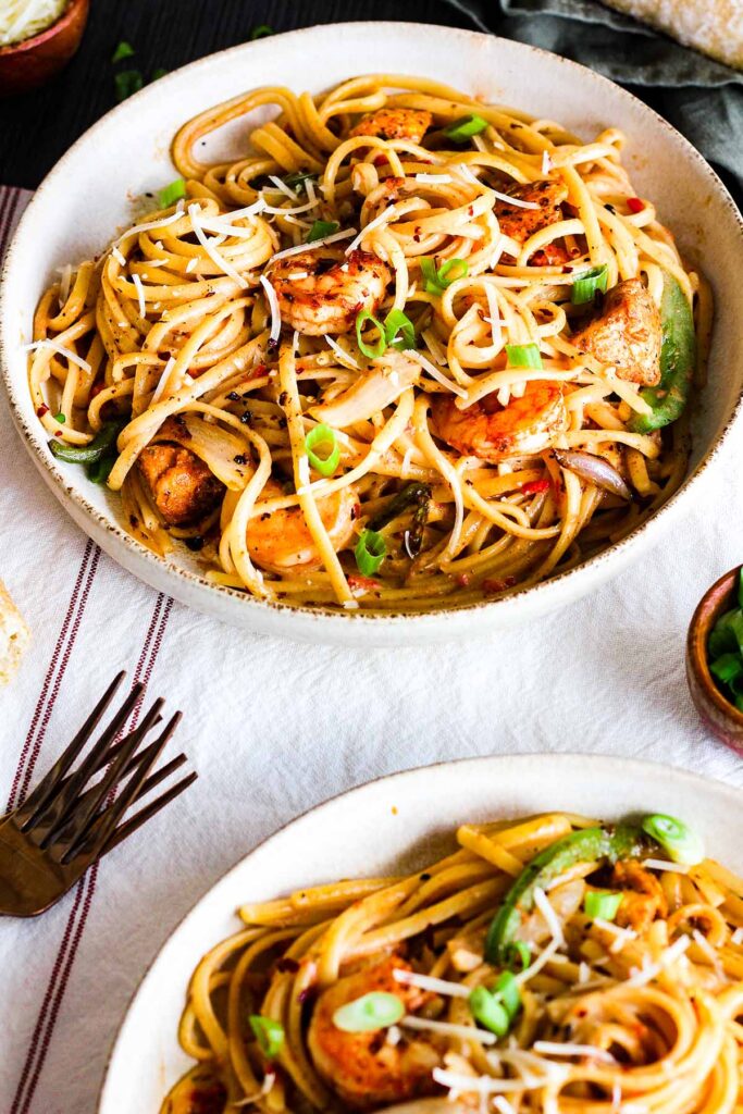 Two bowls of spicy cajun chicken and shrimp pasta with two forks.