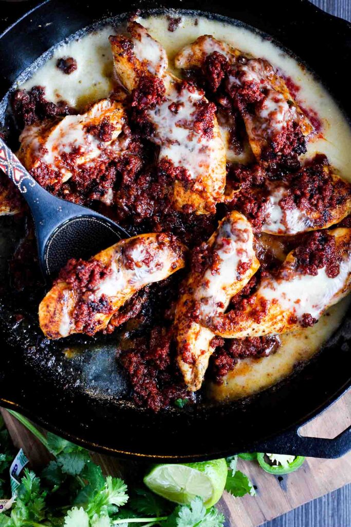 Chicken and chorizo with a spoon in a cast-iron skillet.