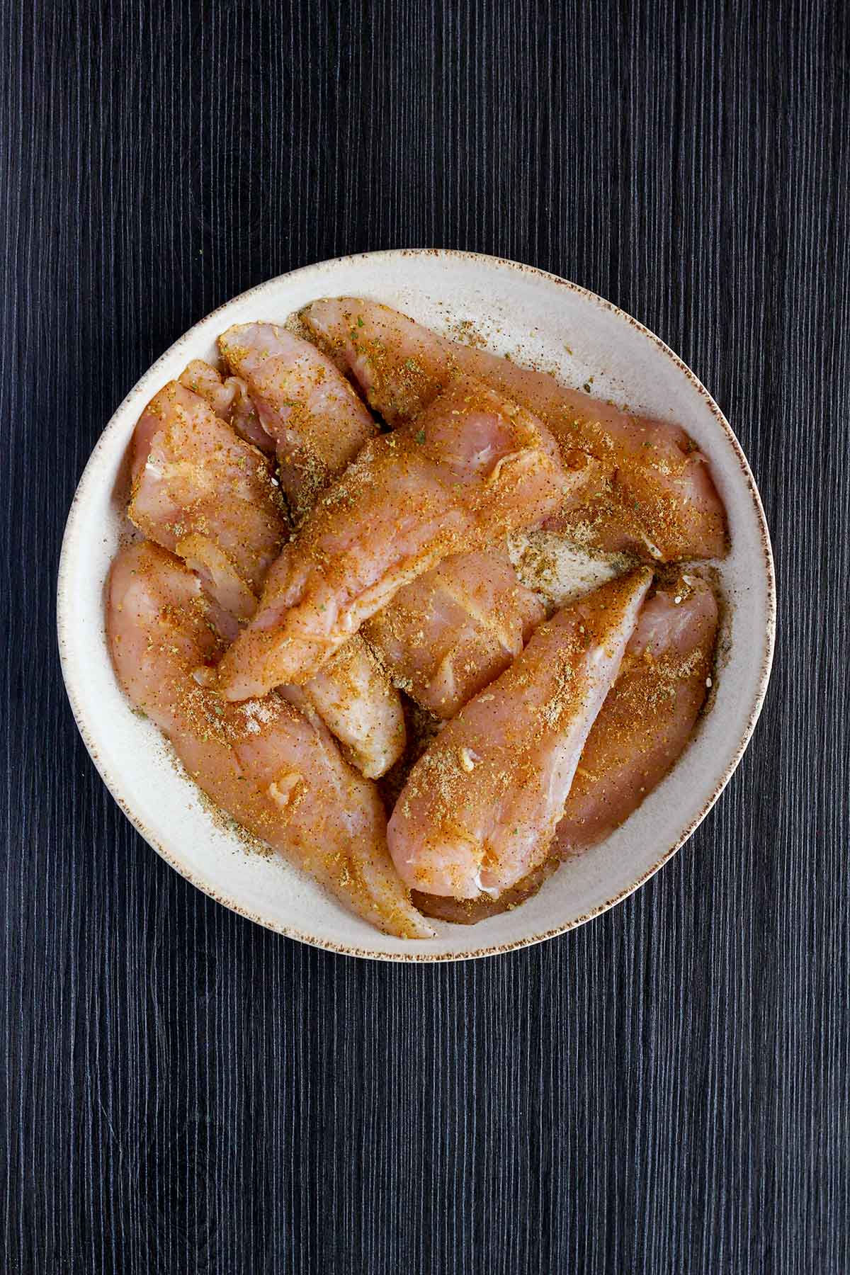Seasoned raw chicken in a bowl.
