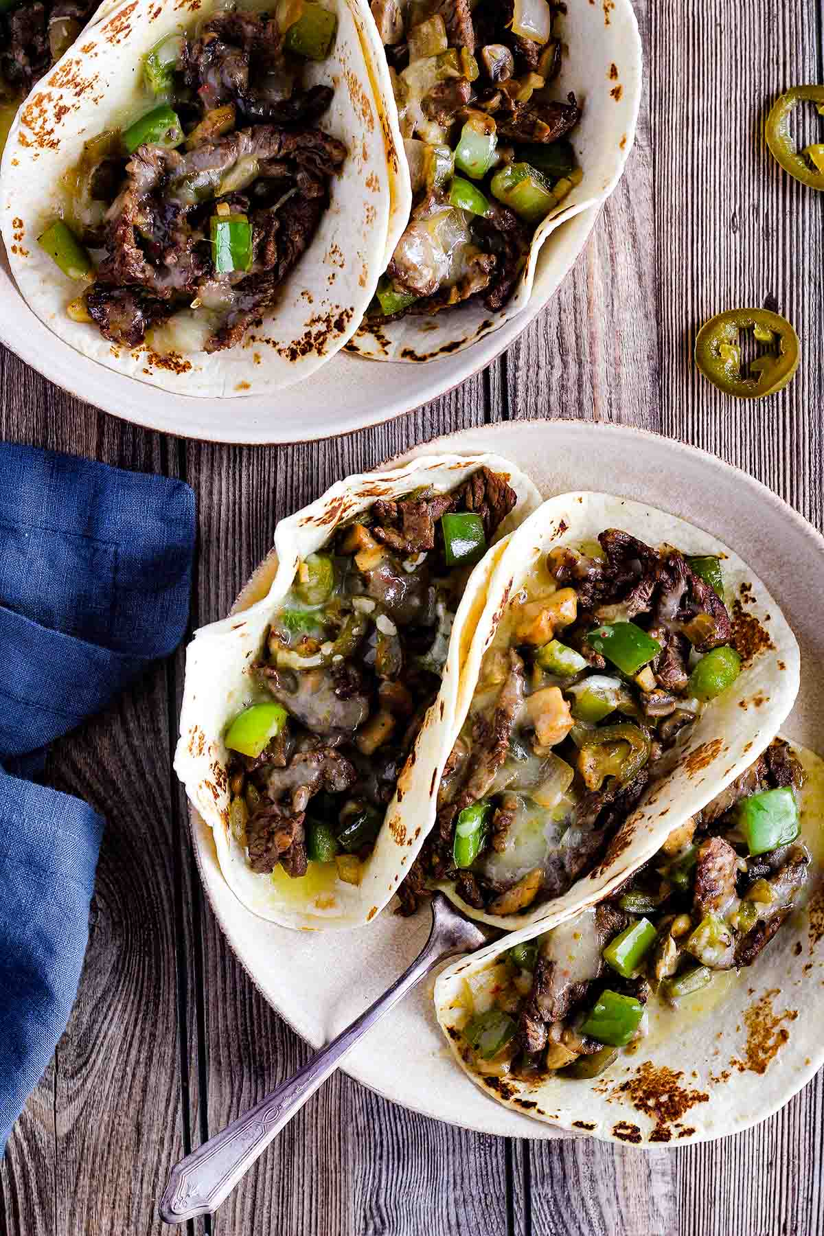 Two bowls of cheesesteak tacos with a fork and jalapenos.