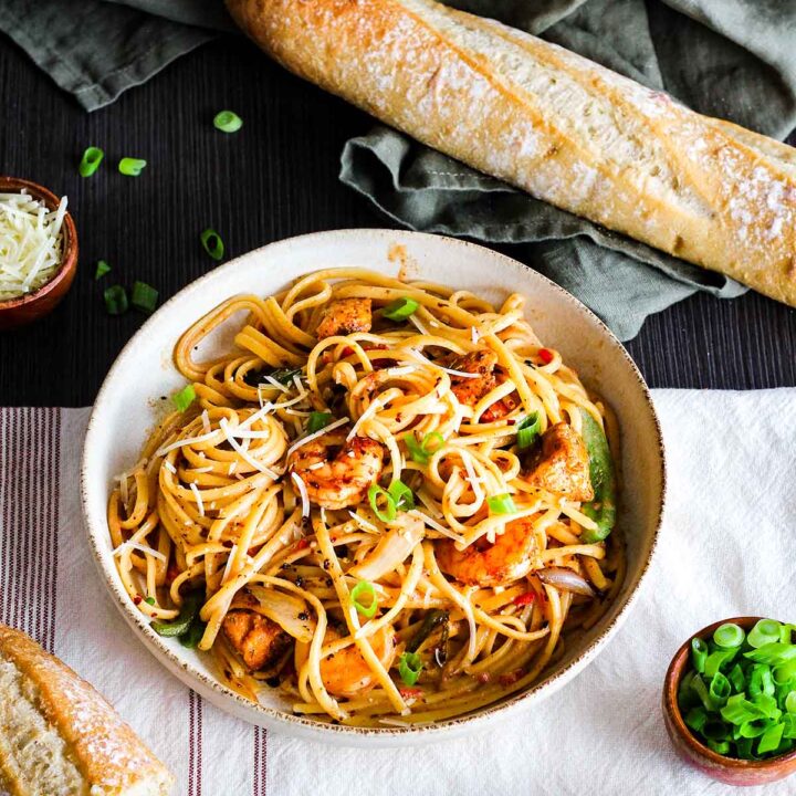 Two bowls of spicy chicken and shrimp pasta with a baguette and side of green onions.