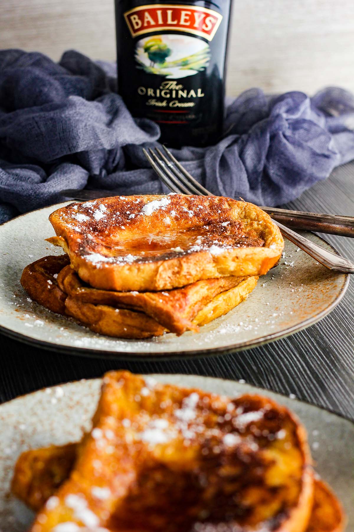 A plate of French toast with a bottle of Baileys in the background.