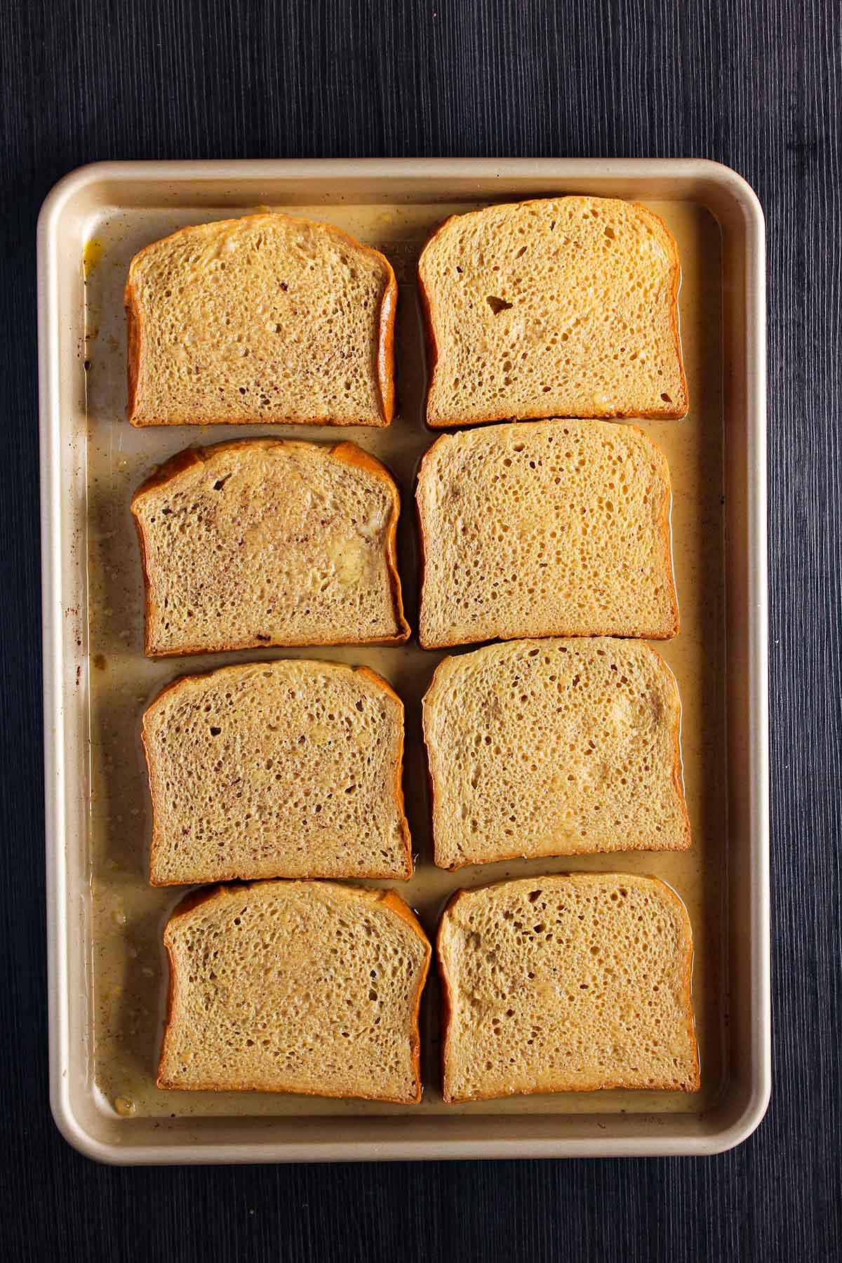 Bread soaking in egg batter in a sheet pan.