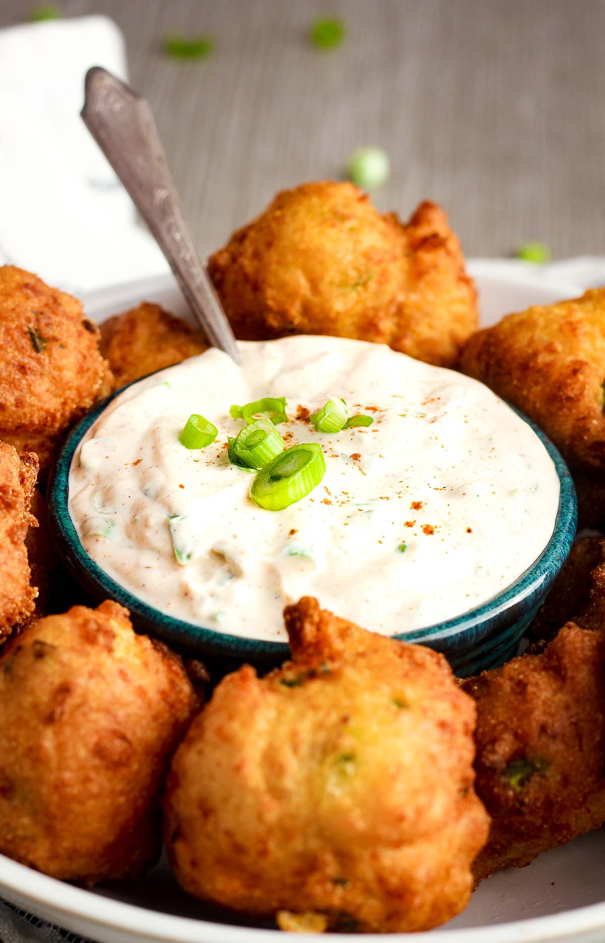 Bowl of Cajun mayo sauce topped with scallions surrounded by hush puppies