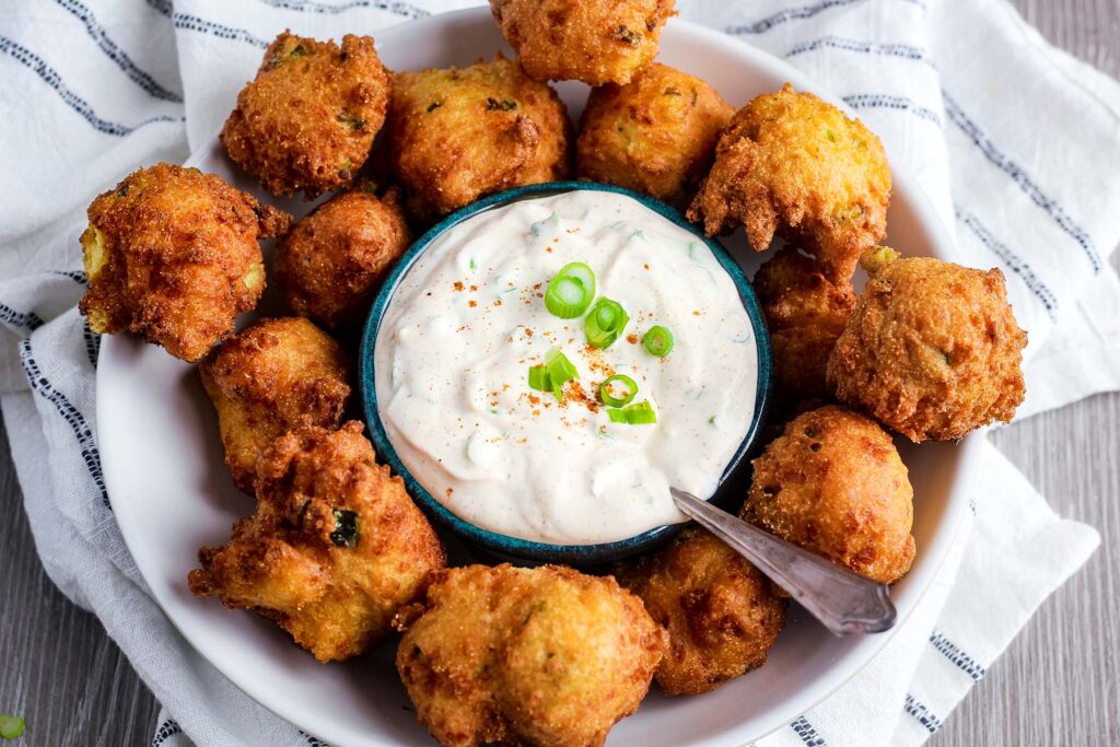 Bowl of hush puppy sauce surrounded by hush puppies on top of a towel