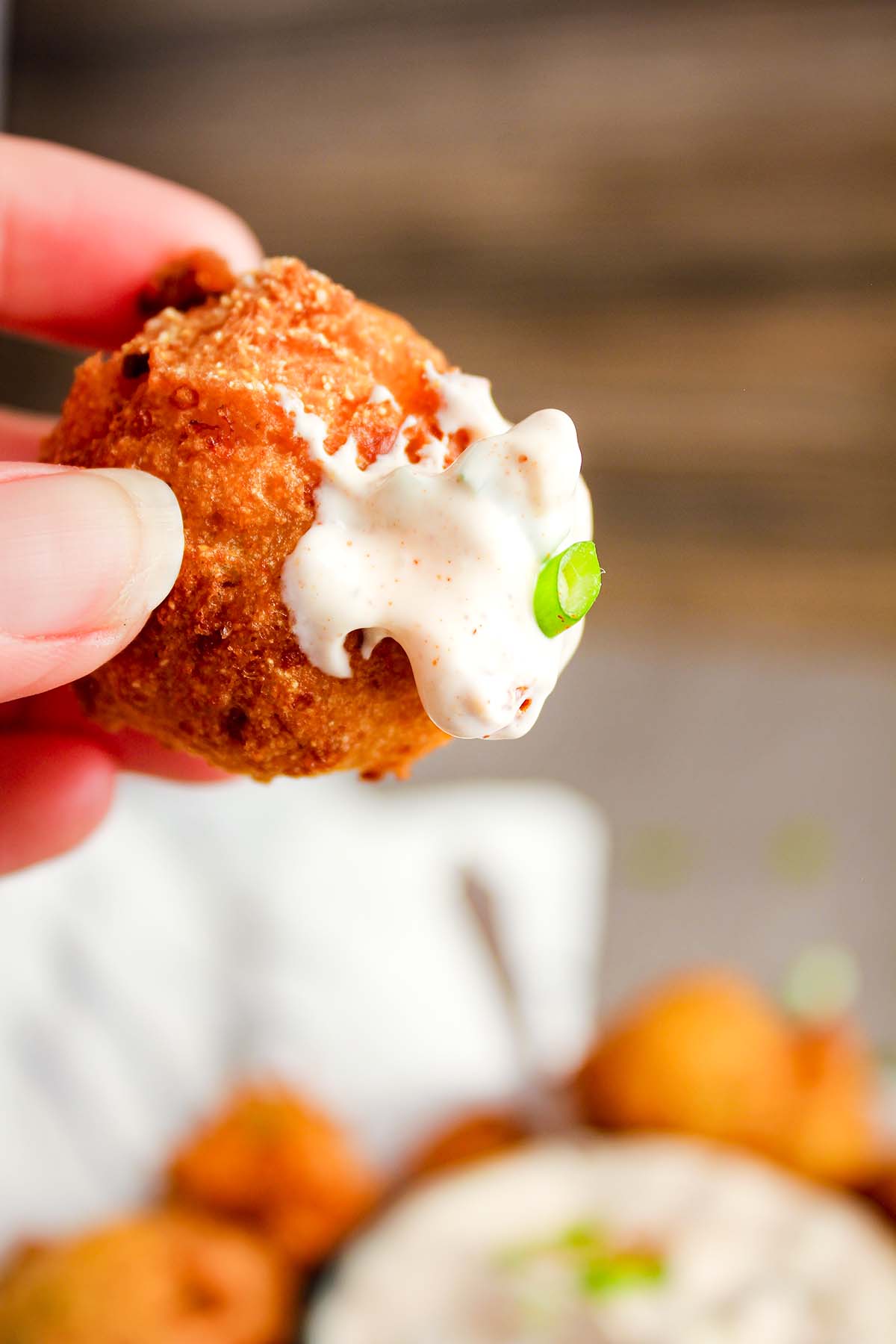 Hand holding hush puppy with Cajun dipping sauce