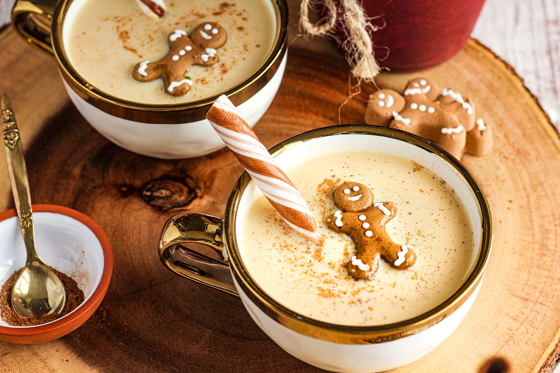 Two cups of eggnog and Baileys on a wood platter with a bowl of spices.