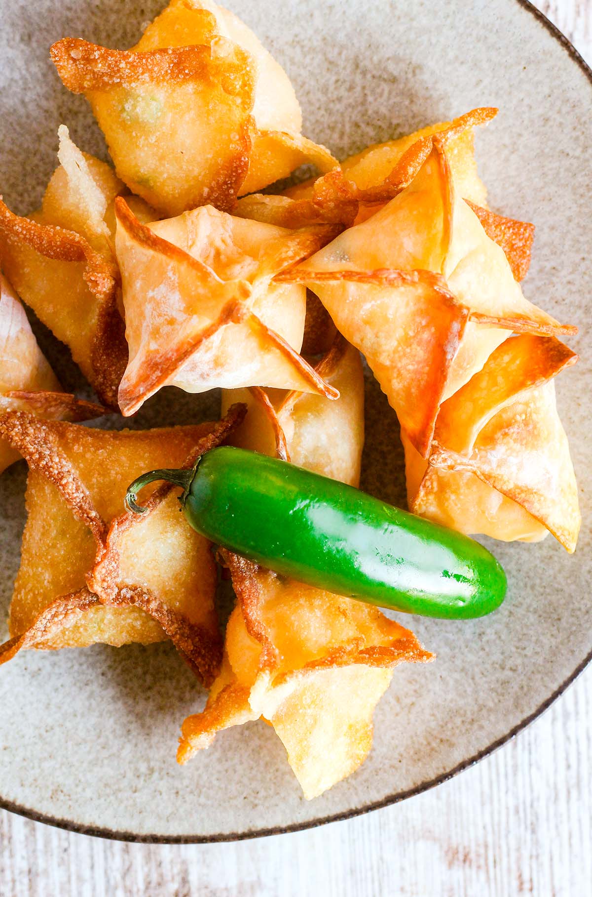 A pile of jalapeno popper wontons on a plate with a whole jalapeno