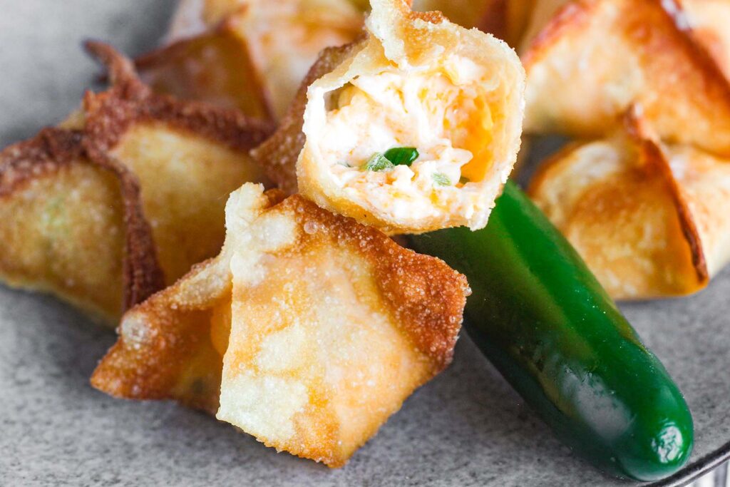 A stack of jalapeno cream cheese wonton poppers one of which is torn open to revel the filling
