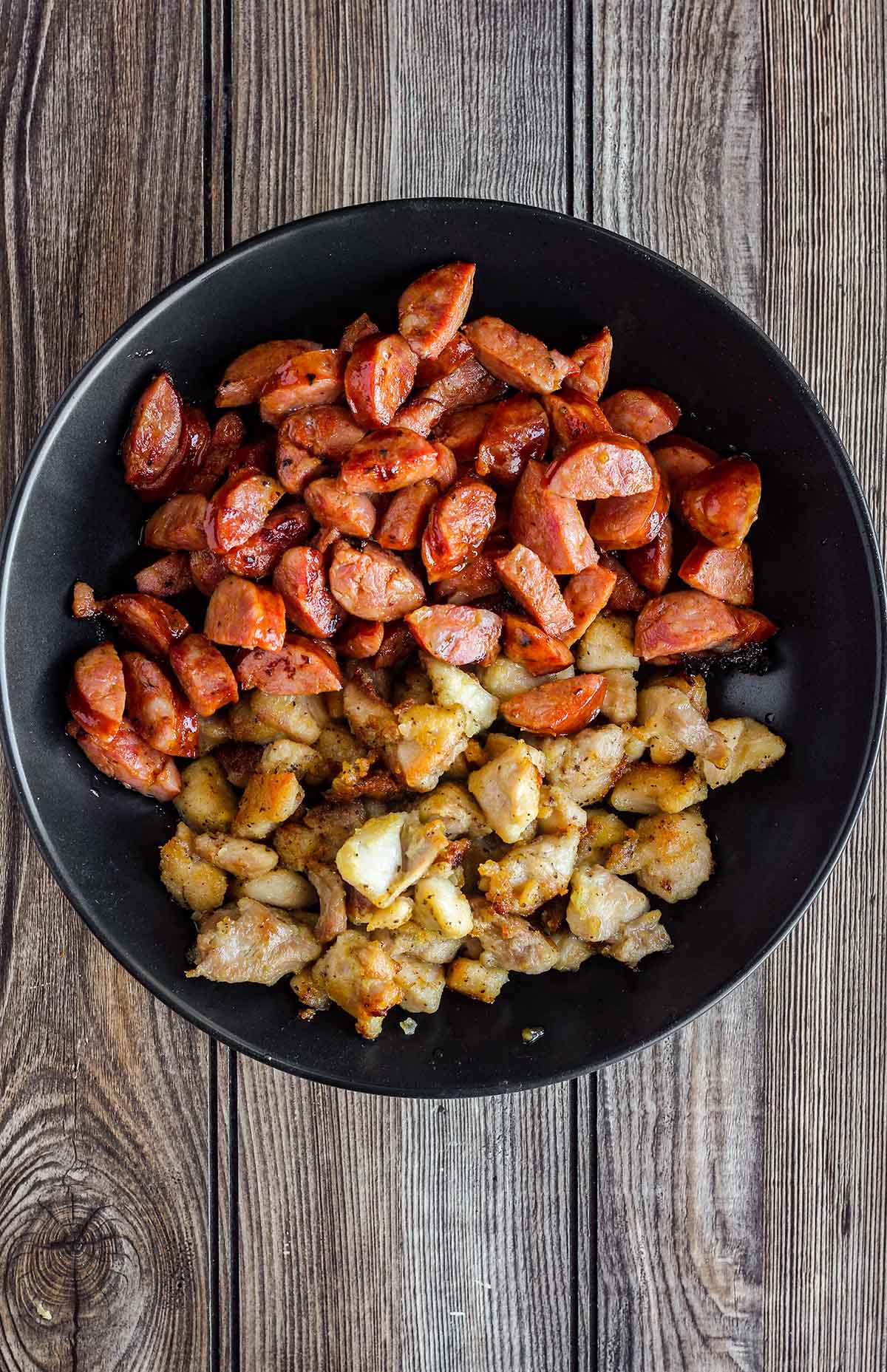 Cooked chicken and andouille sausage in a black bowl