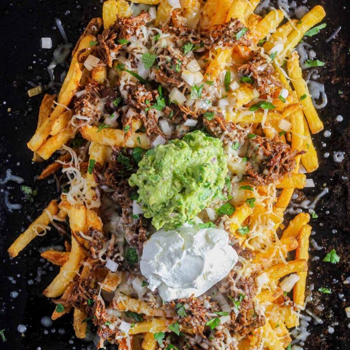 Leftover birria fries toppped with guacamole and sour cream on a sheet pan.