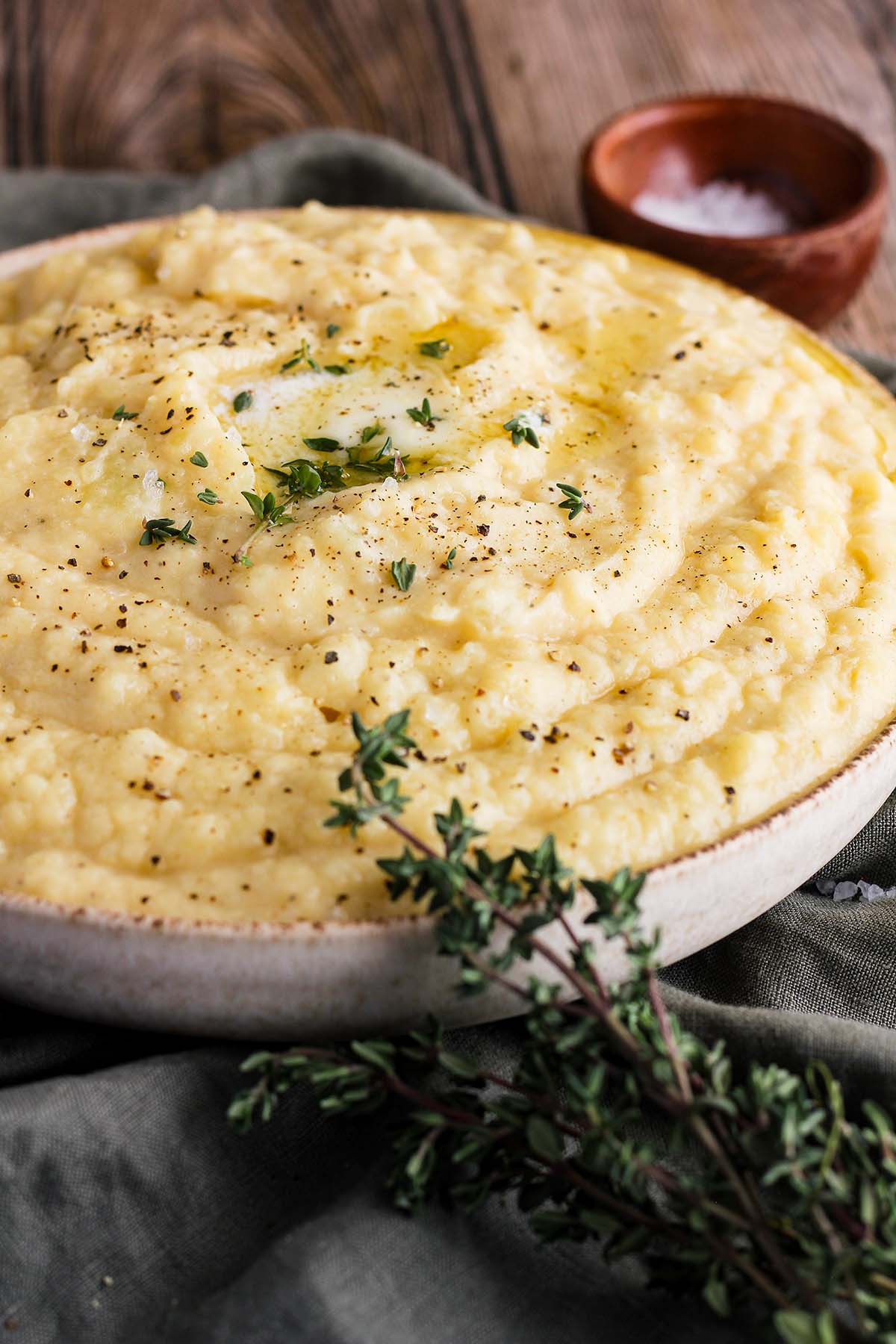 Bowl of mashed potatoes surrounded by a bowl of salt and thyme sprigs.