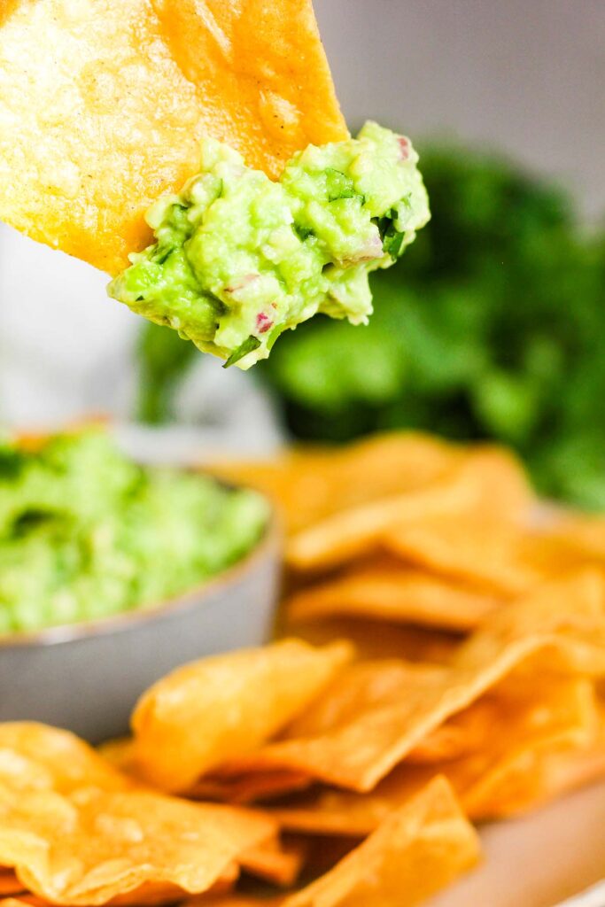 Chip dipped in guac above bowl with chips.