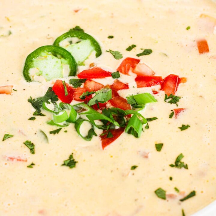 Close-up of 3 cheese queso garnished with cilantro, diced tomato, jalapeno slices, and green onions.