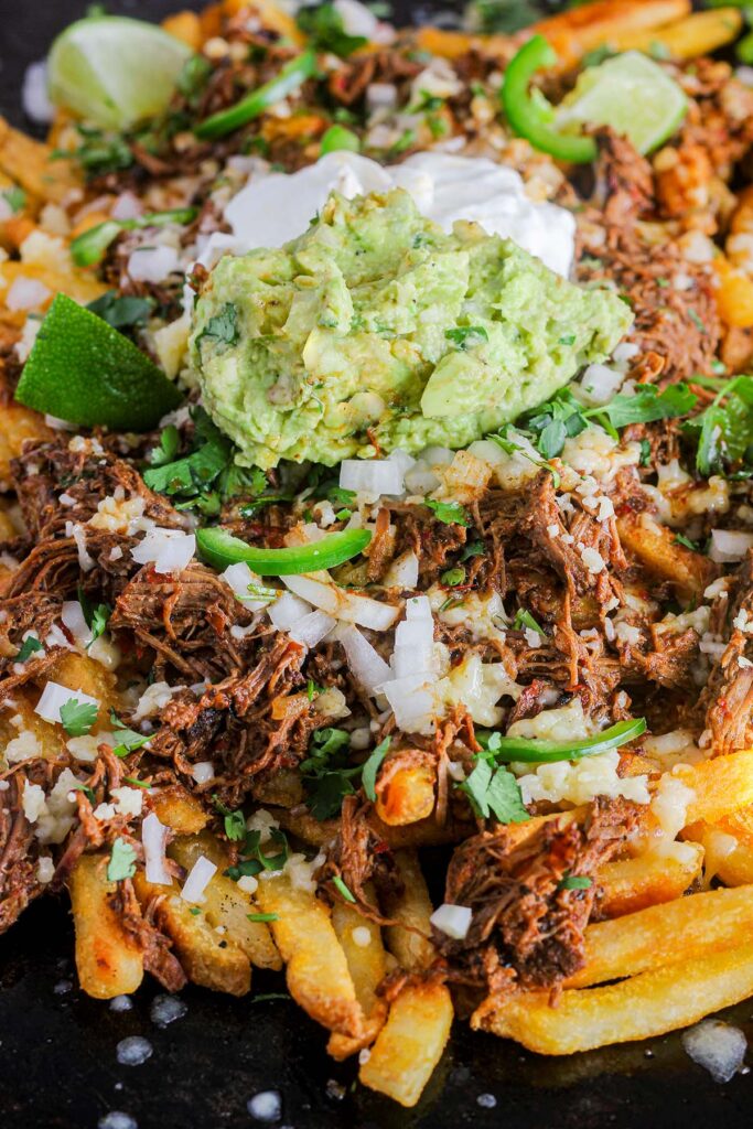 Close up of birria fries topped with guacamole and sour cream.