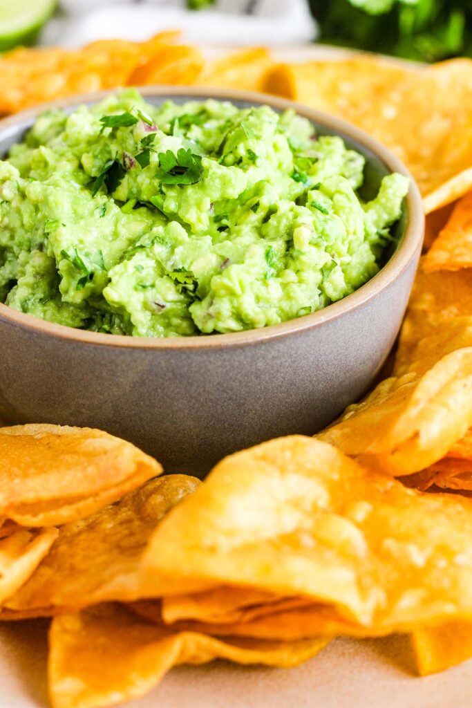 Close up of bowl of guacamole surrounded by chips.