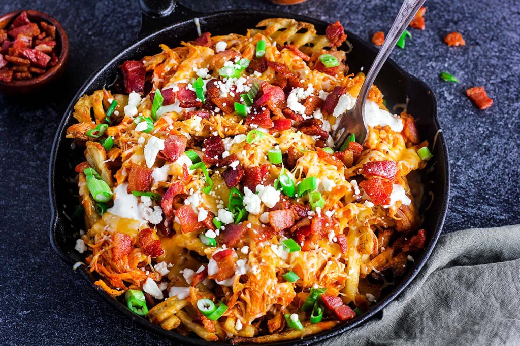 Loaded fries with a fork sticking up and a small bowl of bacon bits.