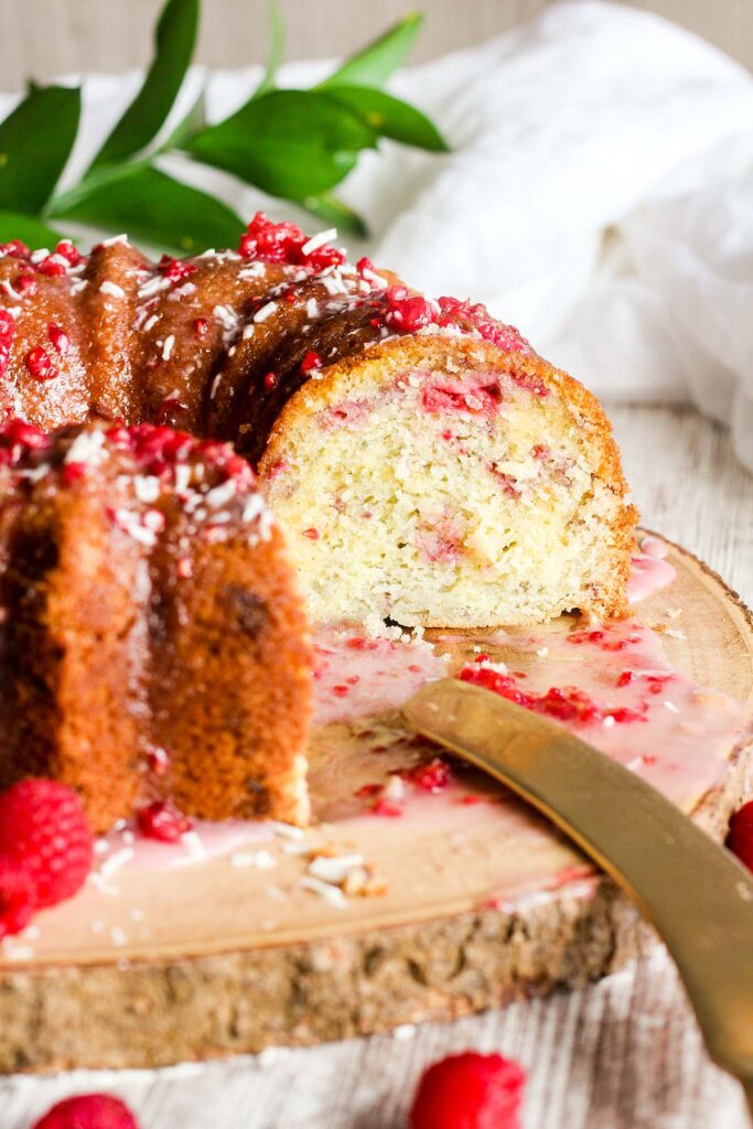 Sliced white chocolate bundt cake with raspberries on a platter with a knife.