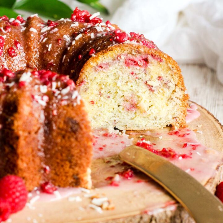 Sliced white chocolate bundt cake with raspberries on a platter with a knife.