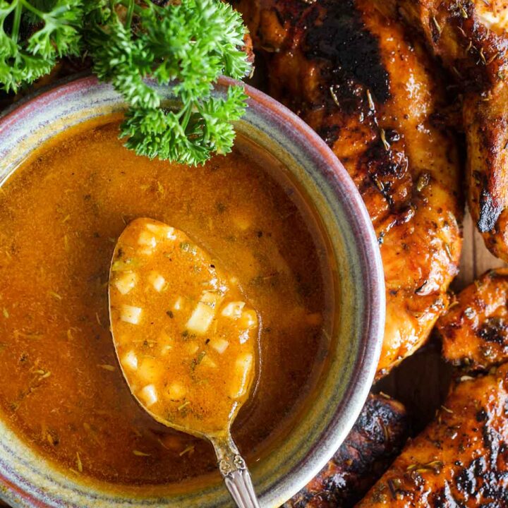 Spoonful of sauce atop a bowl of sauce surrounded by chicken and parsley.