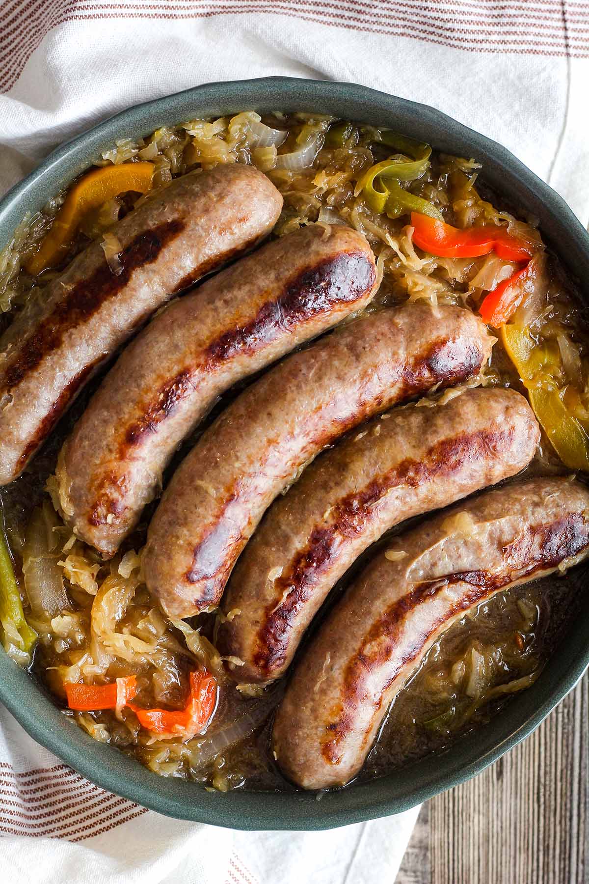 A bowl of brats with sauerkraut, peppers, and onions atop a kitchen towel.