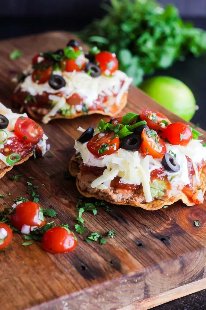 A cutting board topped with three tostadas with cilantro and a lime in background.