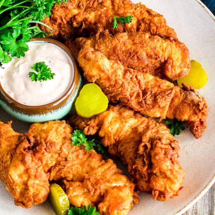 A plate of crispy chicken tenders with ranch, parsley, and pickles.
