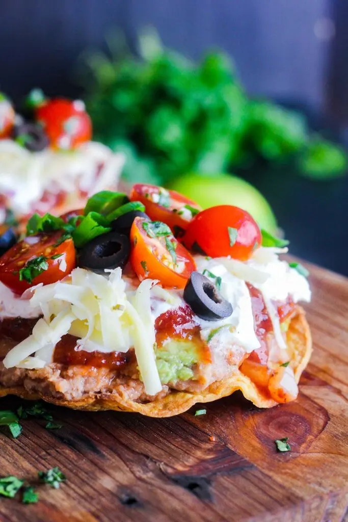 A single seven layer tostada with cilantro and a lime in the background.