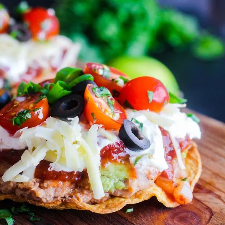 A single seven layer tostada with cilantro and a lime in the background.