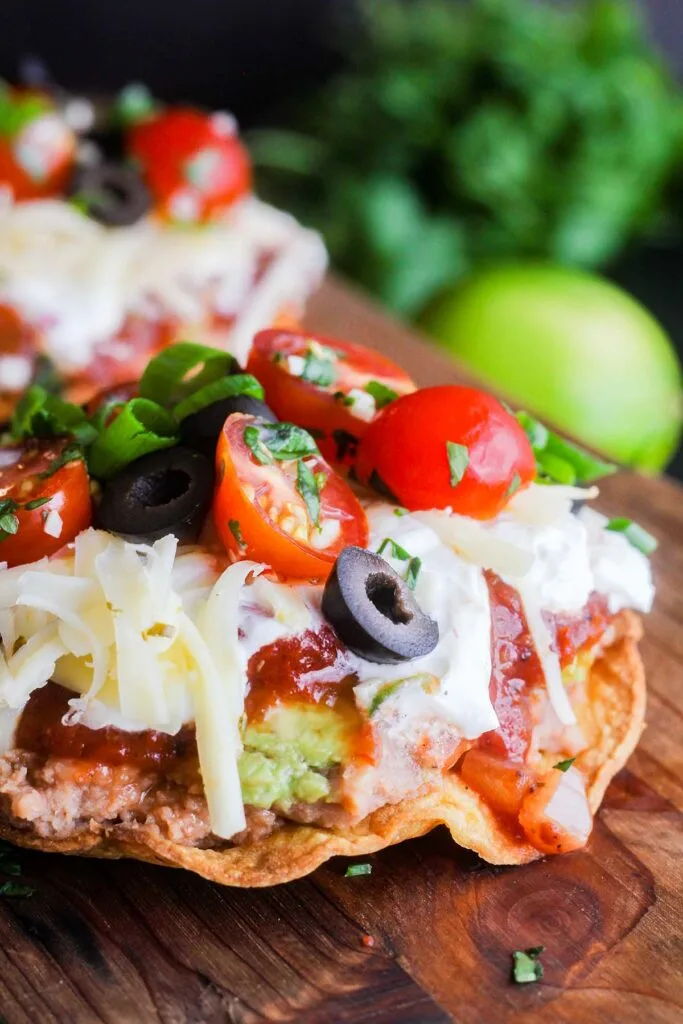 Close up of 7 layer tostada with a bunch of cilantro and a lime in background.