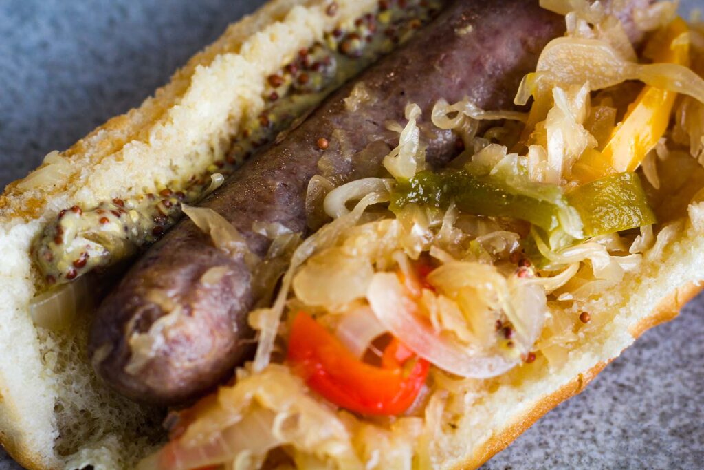 Close up of a brat in a bun with kraut and veggies.