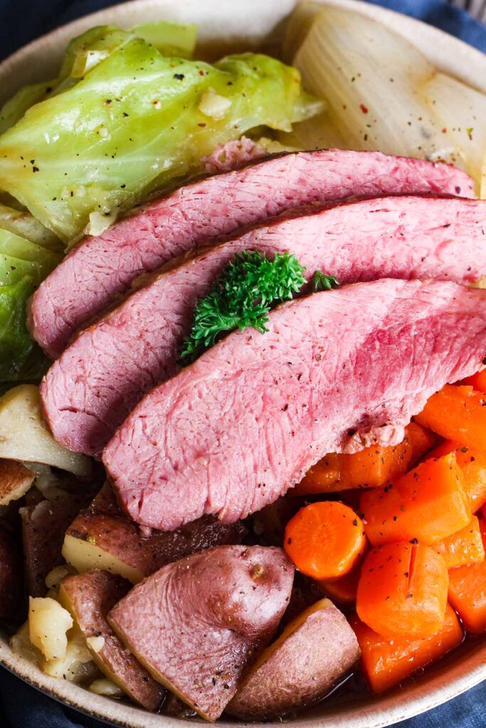 Close up of sliced corned beef atop potatoes, carrots, onion, and cabbage.