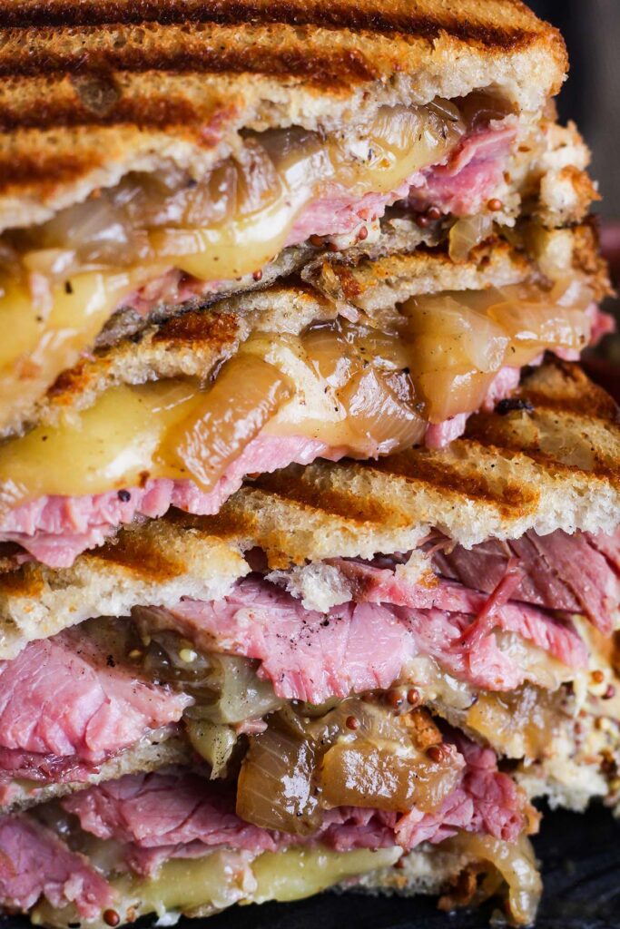 Close up of stacked corned beef on rye sandwiches with Guinness braised onions.