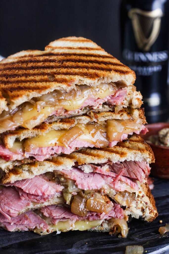 Stacked corned beef sandwich on rye with Guinness stout in background.