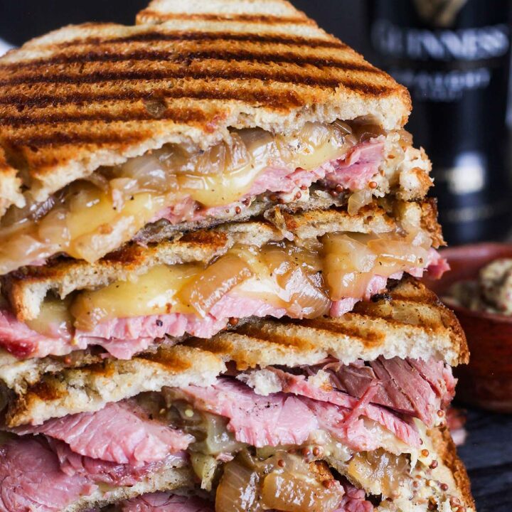 Stacked corned beef sandwich on rye with Guinness stout in background.