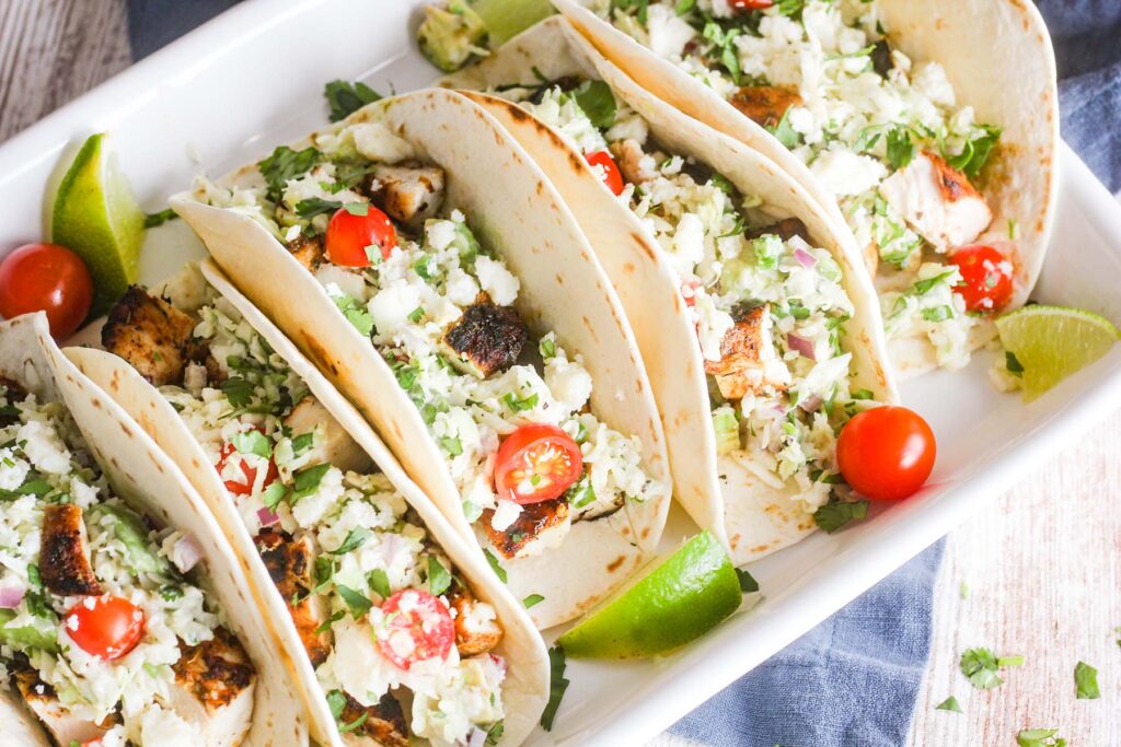 Tray of tacos with lime wedges and cherry tomatoes.