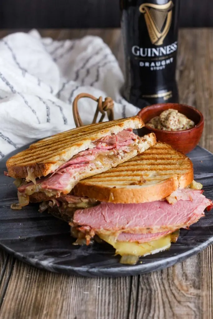 Two halves of corned beef on rye with a side of mustard and a Guinness beer