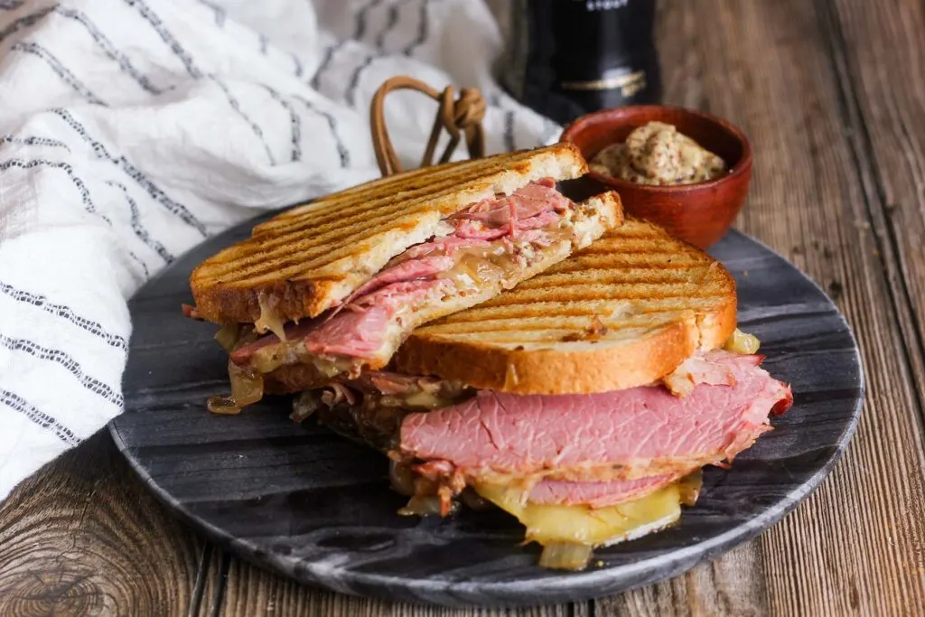Two sandwich halves stacked on a platter with a side of mustard and a white kitchen towel.