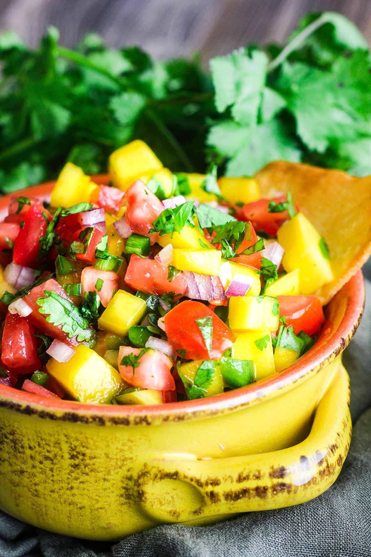 A yellow bowl filled with mango pico de gallo with cilantro in background.