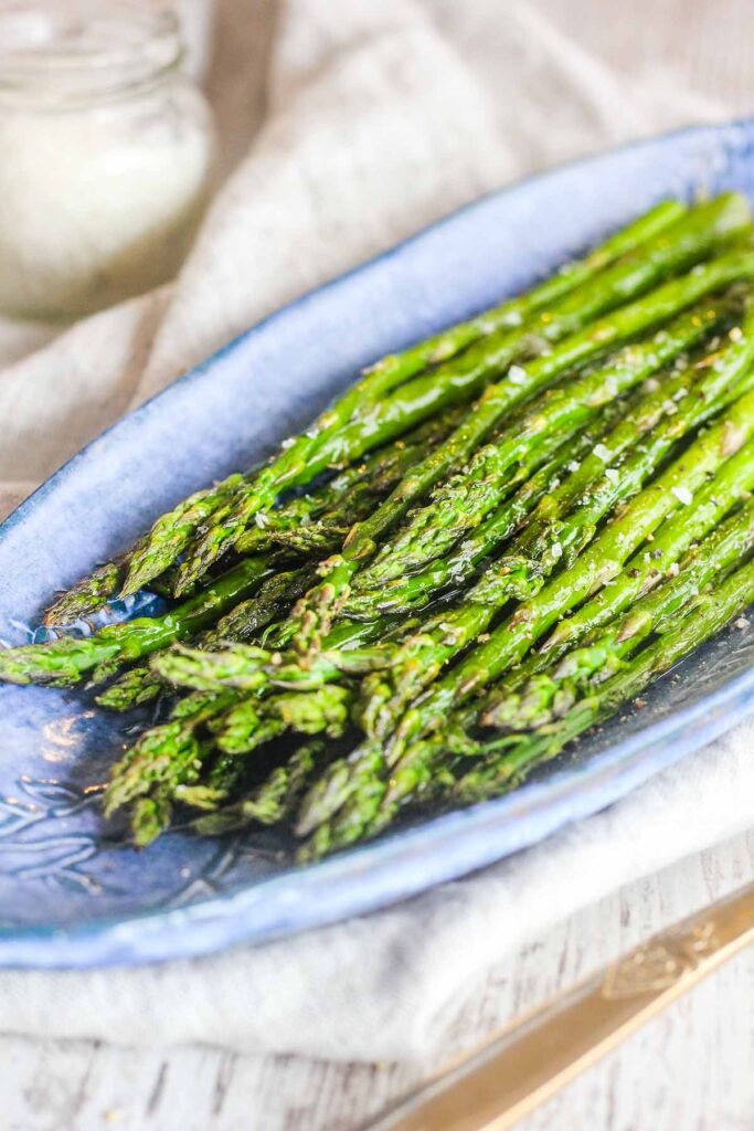 Asparagus on blue dish with a small jar of salt in background.