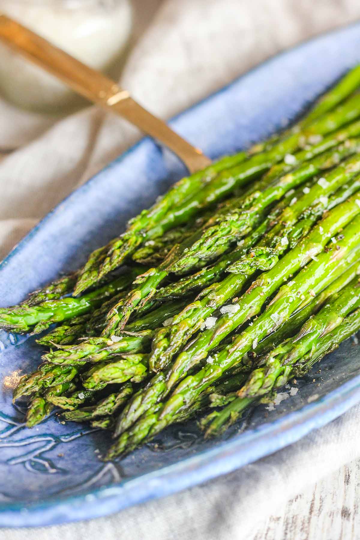 Close up of asparagus on blue serving tray with a gold fork.