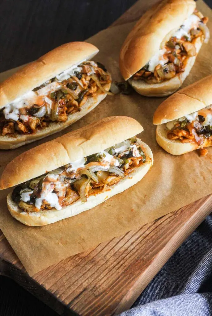 Four buffalo chicken cheesesteak sandwiches on a cutting board.