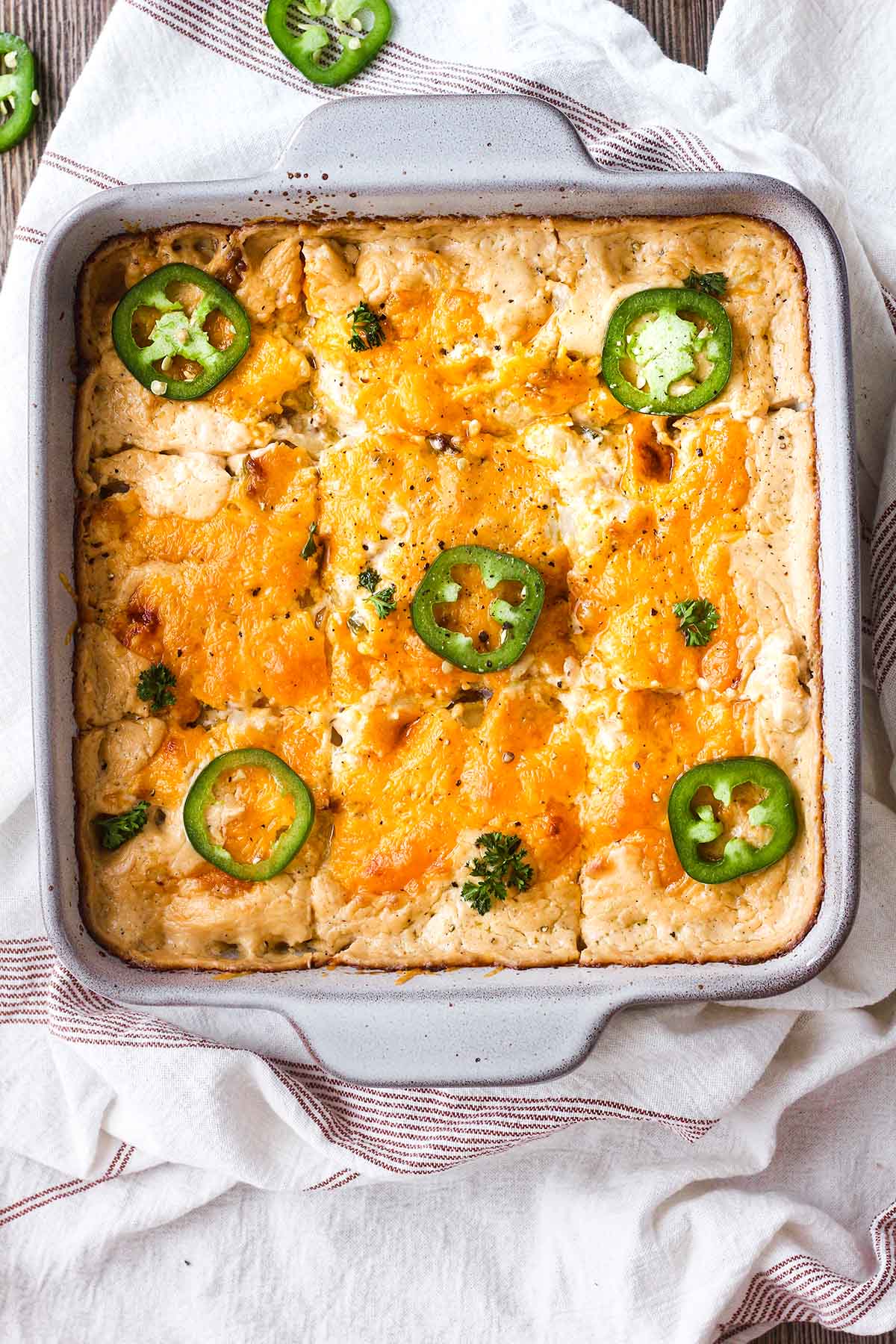 Pan of jalapeno popper cauliflower casserole atop a kitchen towel with scattered sliced jalapenos.