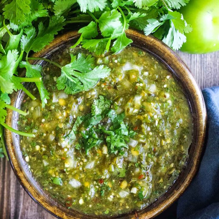 Bowl of salsa with cilantro, tomatillo, and lime halve.