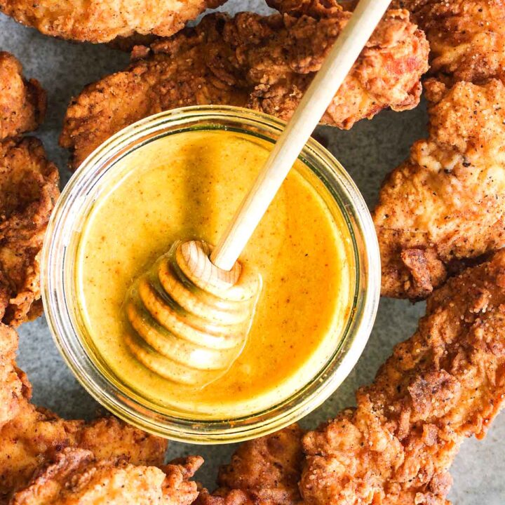 Close up of bowl of honey with honey stick surrounded by crunch chicken tenders.
