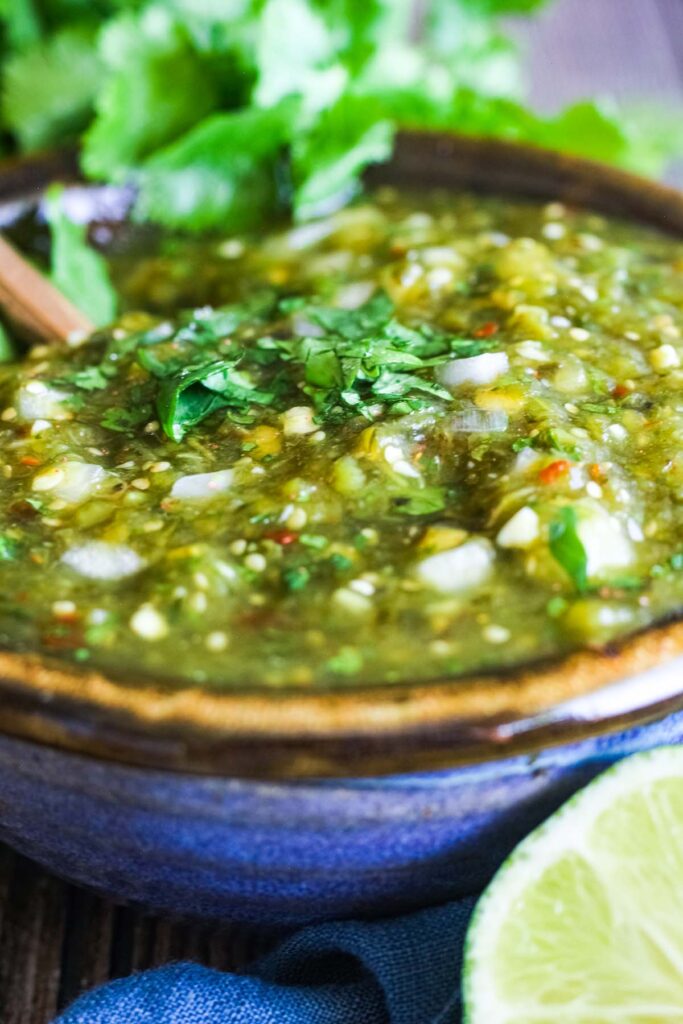 Close up of bowl of salsa verde with cilantro in background.