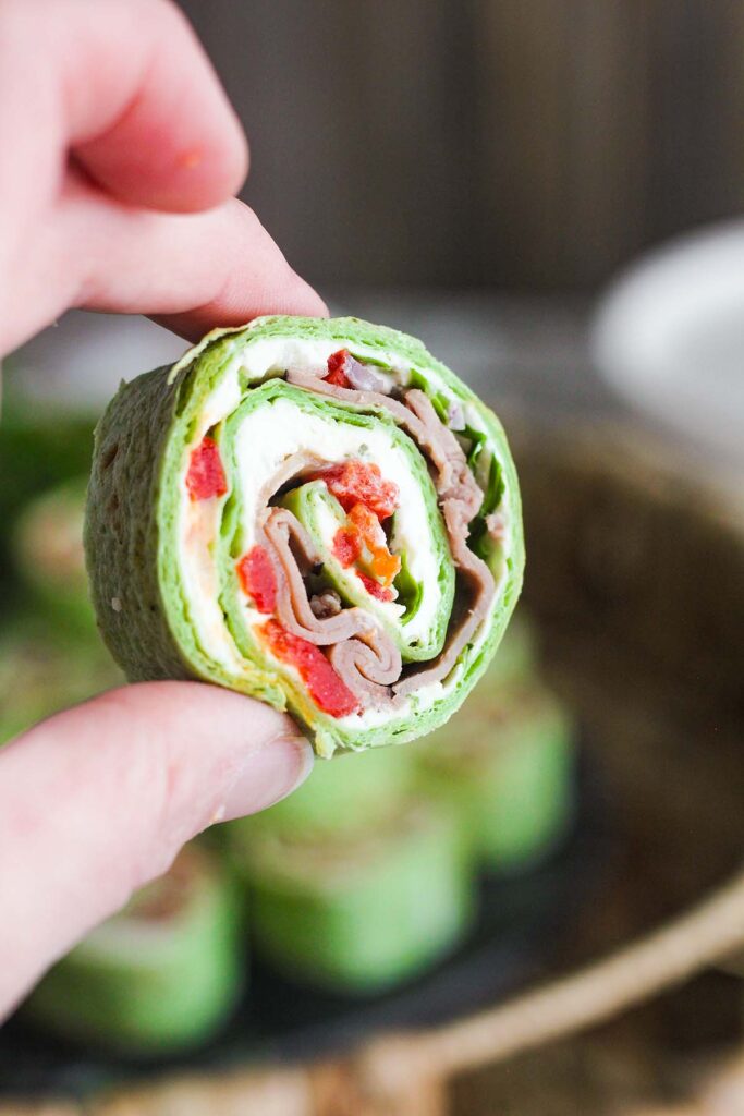Close up of hand holding a single roast beef pinwheel.