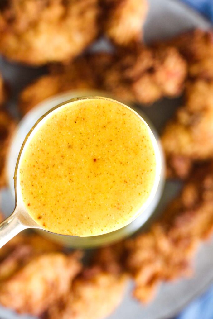 Close up of spoonful of honey mustard with chicken in background.