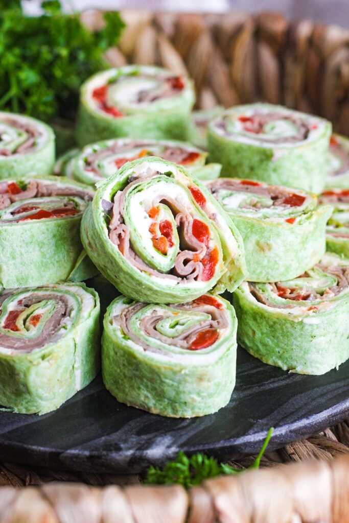 Close up of stack of roast beef pinwheels on a tray with parsley in background.